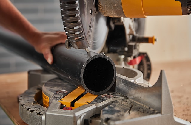 Person cutting a PVC pipe with a mitre saw