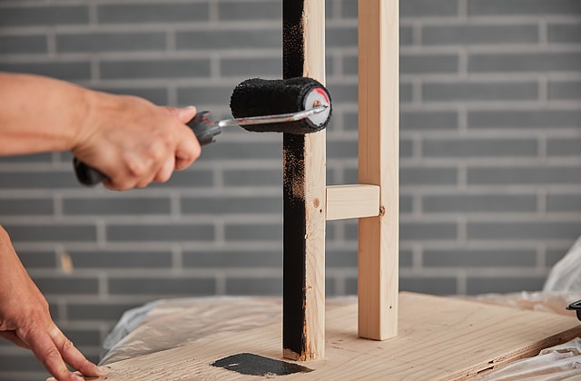 Person painting a stand black with a roller