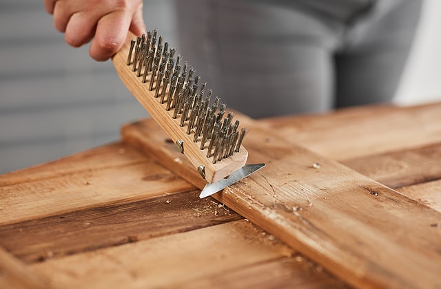 Personne en train d’abîmer des planches de bois avec un grattoir