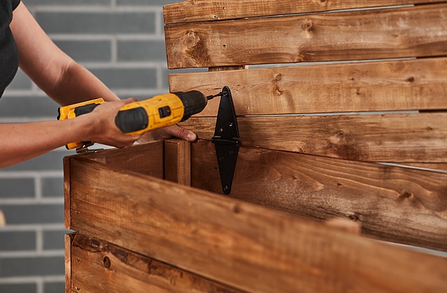 Person securing black hinges onto a wooden coffin