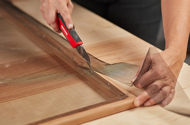 Person cutting mesh screen with a utility knife