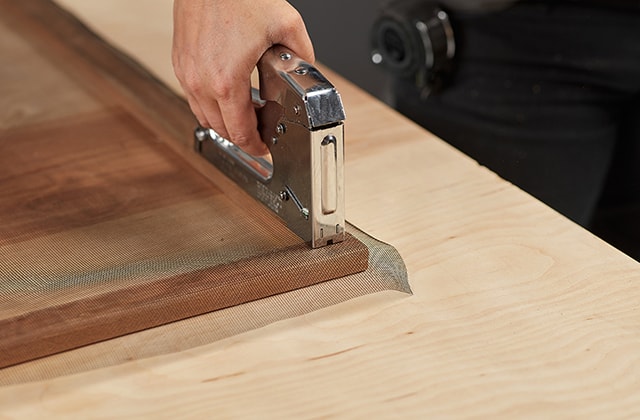 Person securing mesh creen to a wooden frame with a stapler