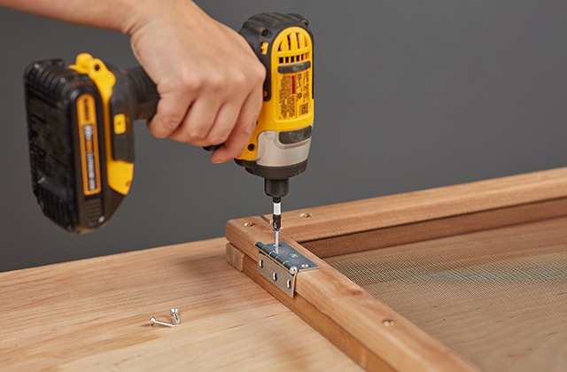 Person adding hinges to a wood and mesh frame