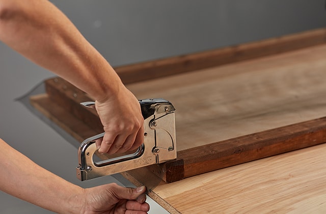 Person securing mesh screen to a wooden frame