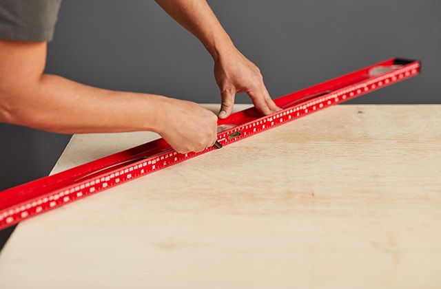 Person tracing a line on a plywood sheet