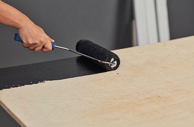 Person painting a plywood sheet black