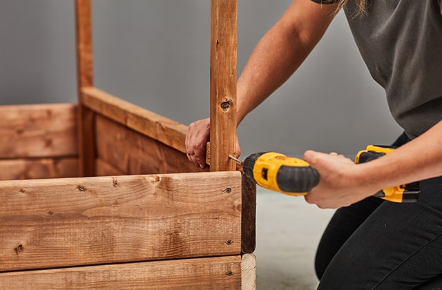 Personne fixant une pièce de bois sur une jardinière