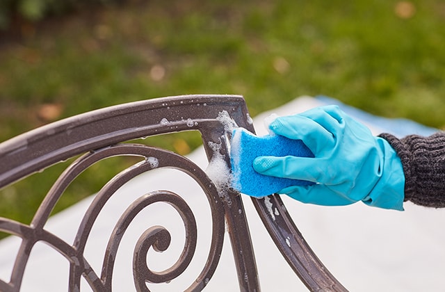 Personne nettoyant des meubles de jardin avec une éponge