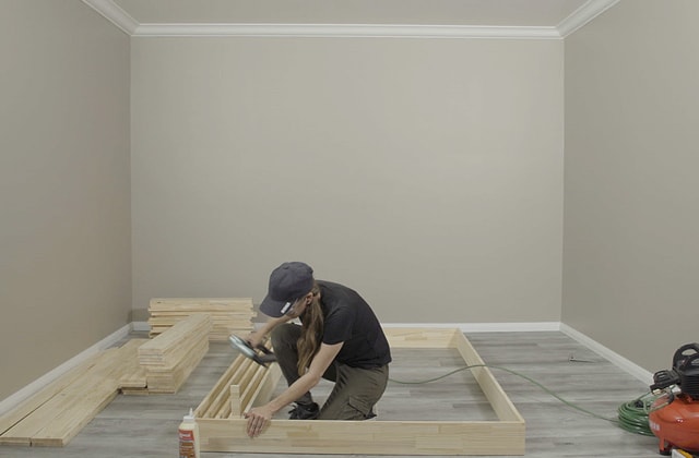 Personne qui assemble une structure en bois sur le plancher