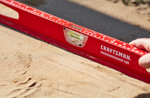 Personne vérifiant qu’une surface de sable est de niveau