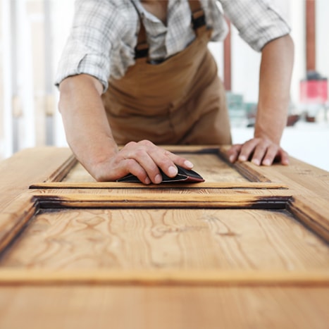 Homme sablant une porte en bois