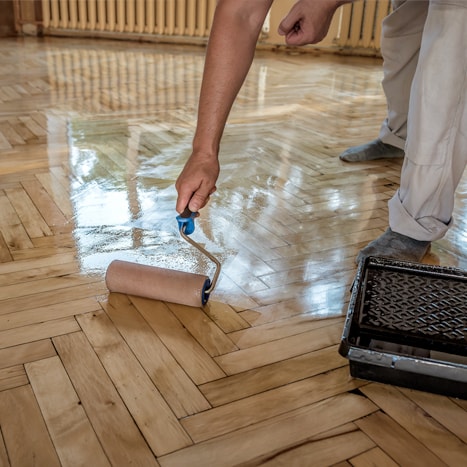 Person applying varnish on a wooden floor with a roller