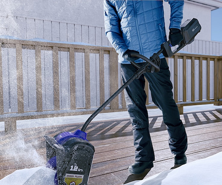 Man using an electric snow shovel on a deck