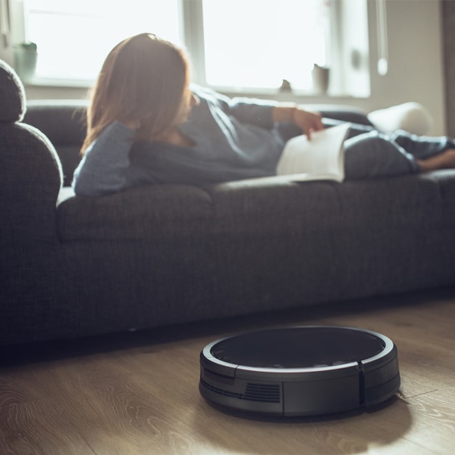 Femme couchée sur un divan avec un robot aspirateur