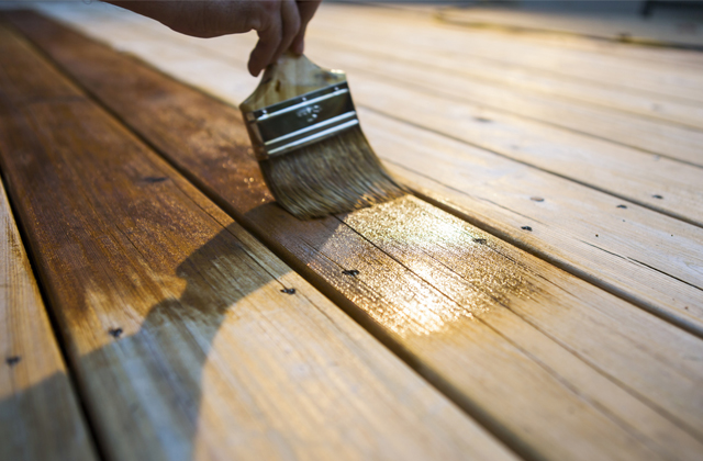 Personne appliquant de la teinture sur une terrasse en bois